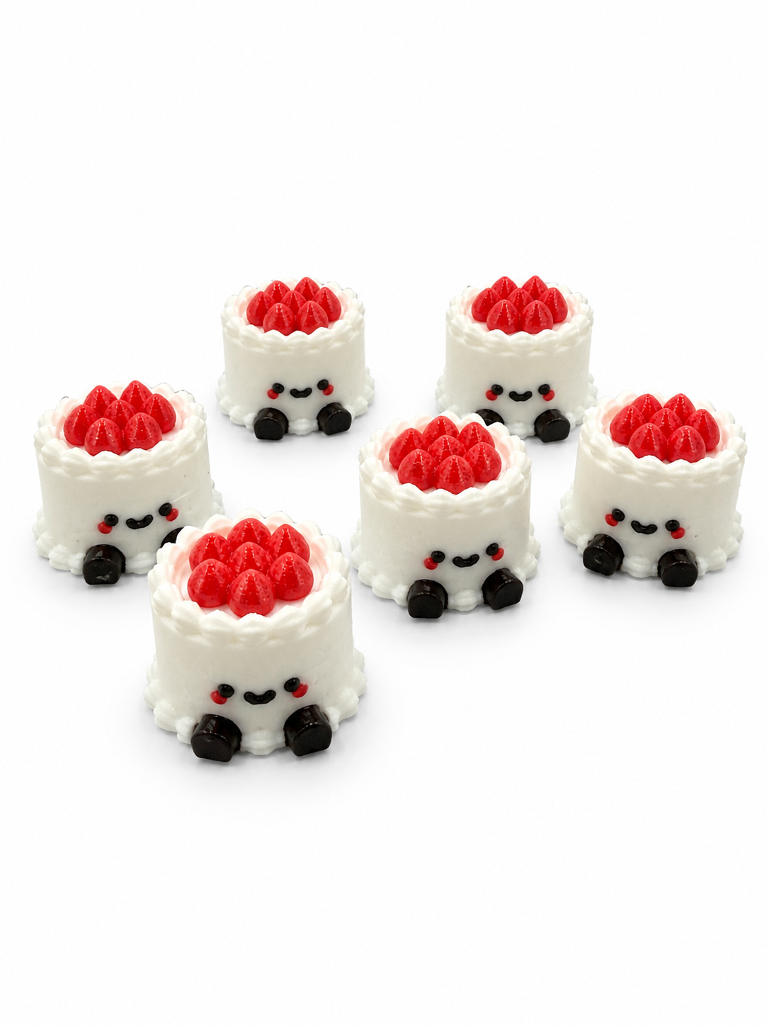 Six small cake-shaped keychains with smiling faces, white frosting, red strawberries on top, and black feet, arranged on a white background.