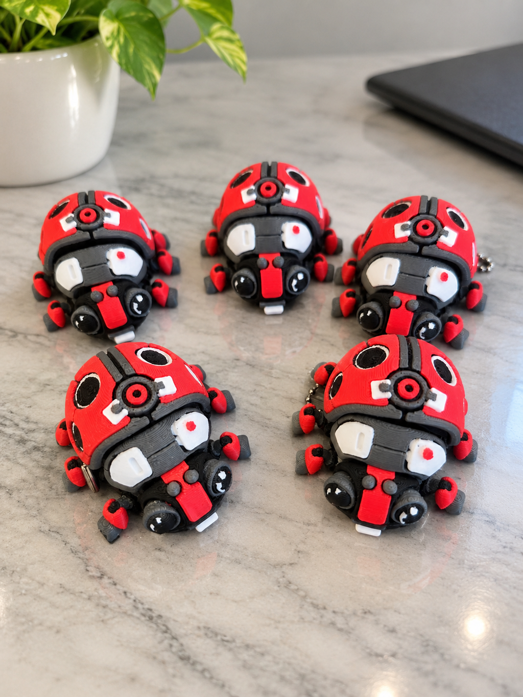 Ladybug-shaped clicker toys in red, black, and white, arranged on a marble surface with a plant and laptop in the background.